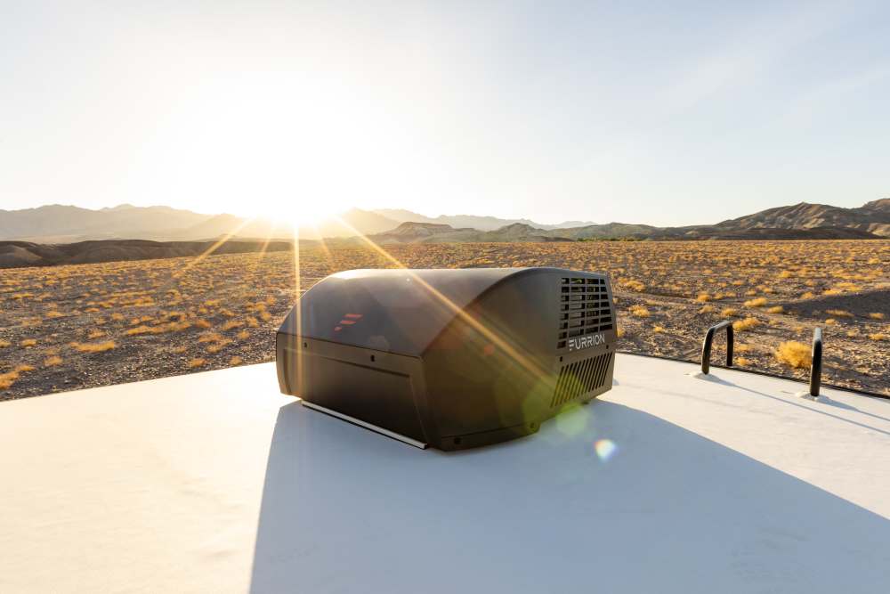 A close view of the top of a travel trailer showing a rooftop air conditioner shroud and roof vents under daylight