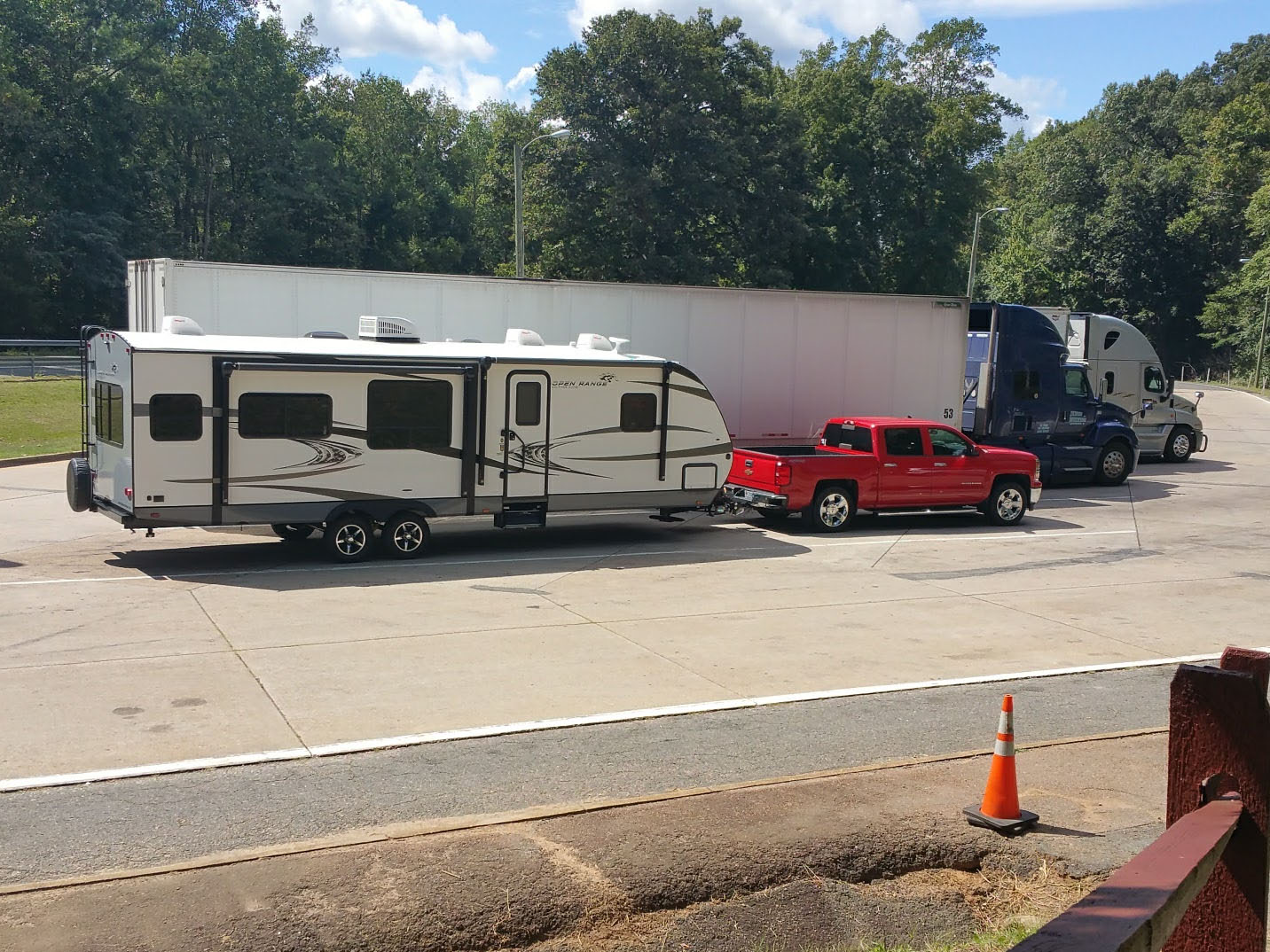 A pickup truck and travel trailer parked in a spacious interstate rest area parking bay with plenty of room around the rig in daylight