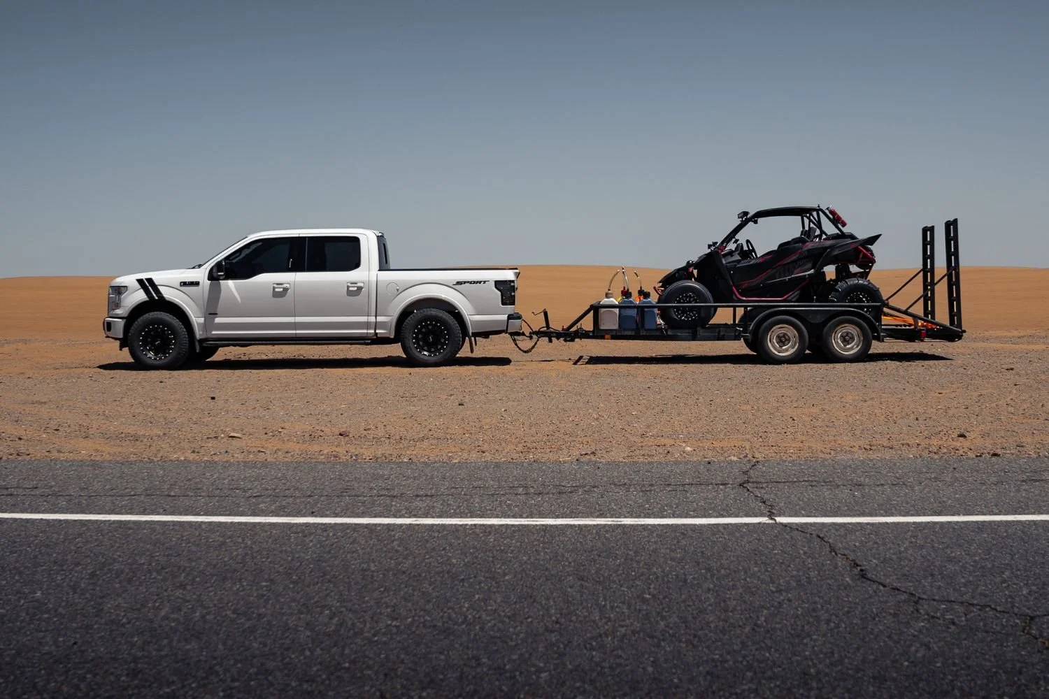 A pickup truck hitched to a travel trailer parked on a flat driveway while a helper stands near the trailer side, ready to guide mirror adjustments