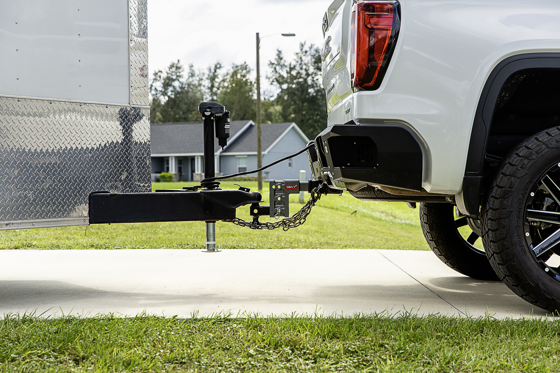 A pickup truck lined up with a bumper-pull trailer on a flat driveway, with the trailer coupler positioned above the hitch ball and the tongue jack supporting the trailer