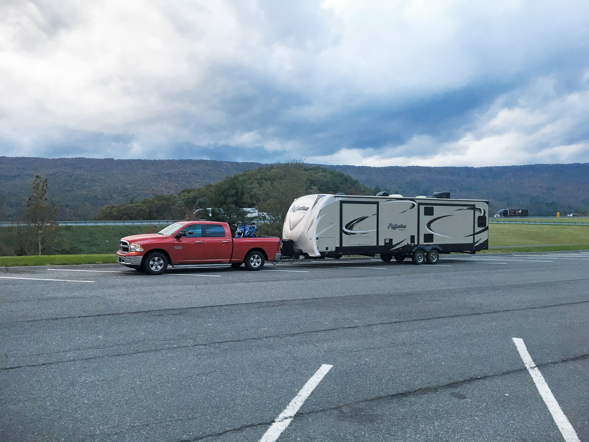 A pickup truck towing a travel trailer on a divided highway in daylight with overhead bridges visible in the distance