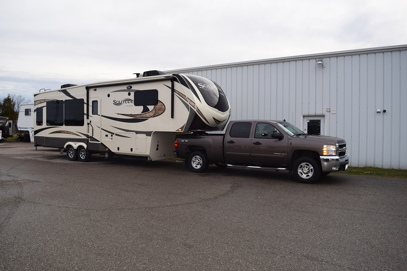 A pickup truck towing a travel trailer viewed from behind at an angle, showing both trailer sides and the truck mirrors extended