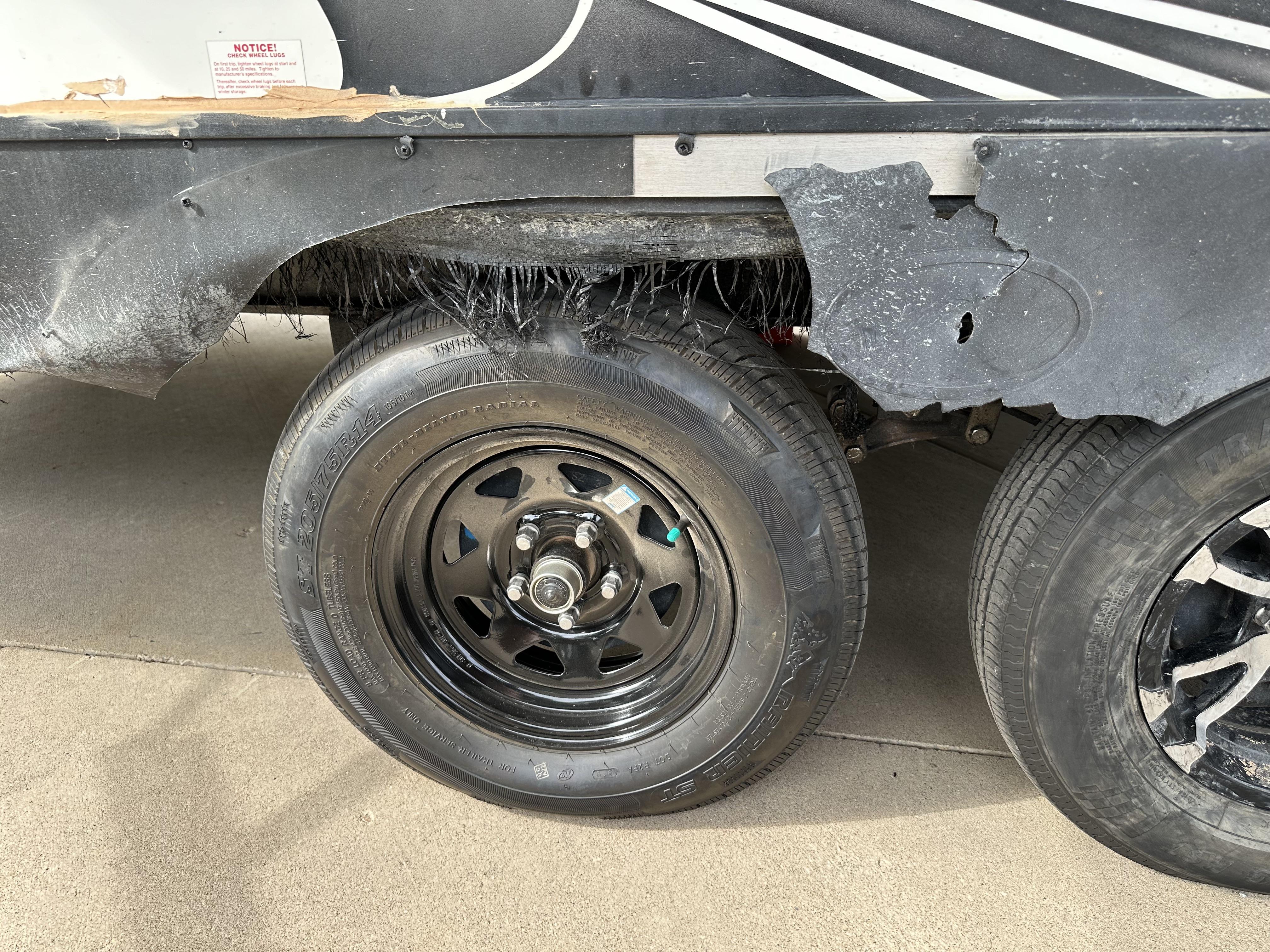 A tandem axle trailer parked on pavement with rubber debris and scuffing visible inside the wheel well near one axle during an inspection