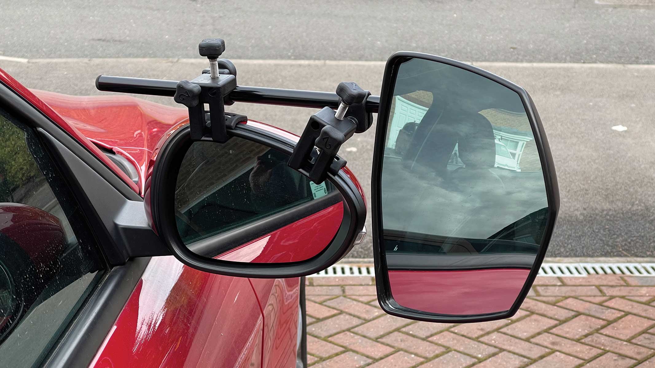 Close view of a towing mirror with a smaller convex spot mirror being adjusted by hand on a pickup truck