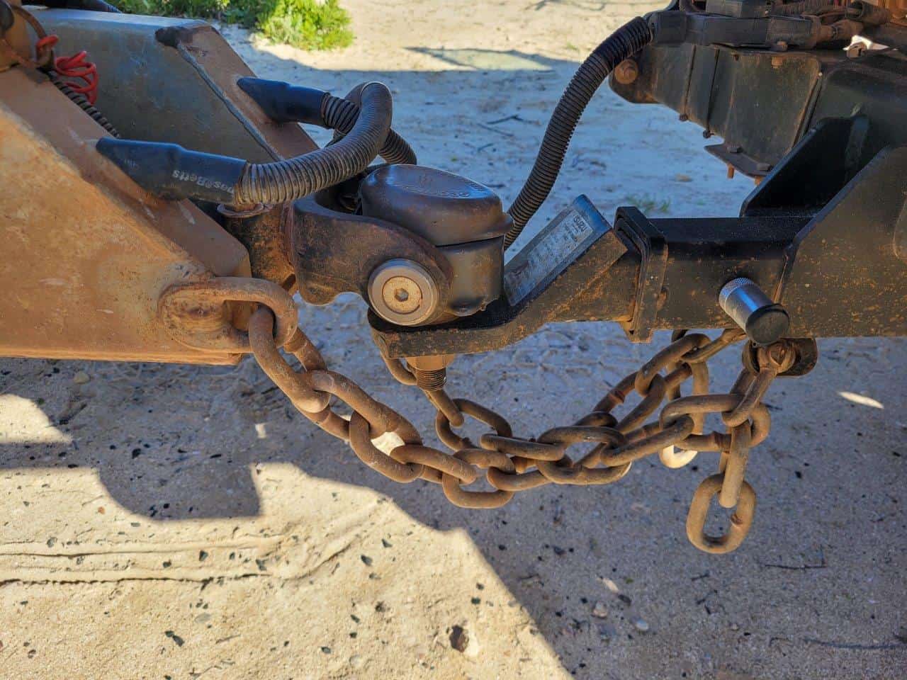 Crossed safety chains forming an X under a trailer coupler, hooked to safety-chain attachment points near a pickup truck receiver